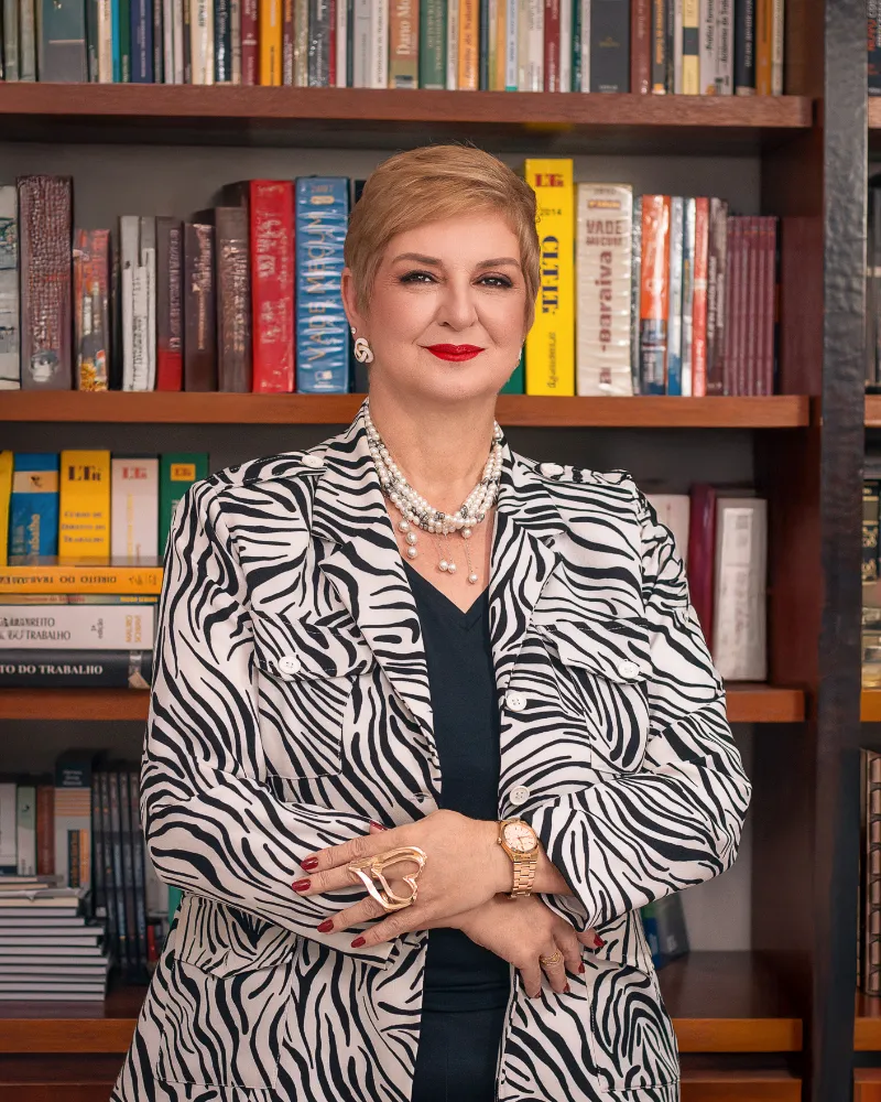 Dra. Donatila Bertola diante da estante de livros do escritório